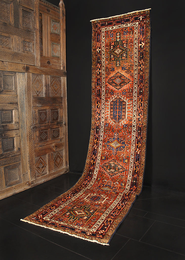 Karaja runner from Northwest Iran woven during second quarter of 20th century. Pattern of alternating geometric shapes and hooked lozenges on rust colored field. Indigo blue and greens are offset by soft ivory tones. 
