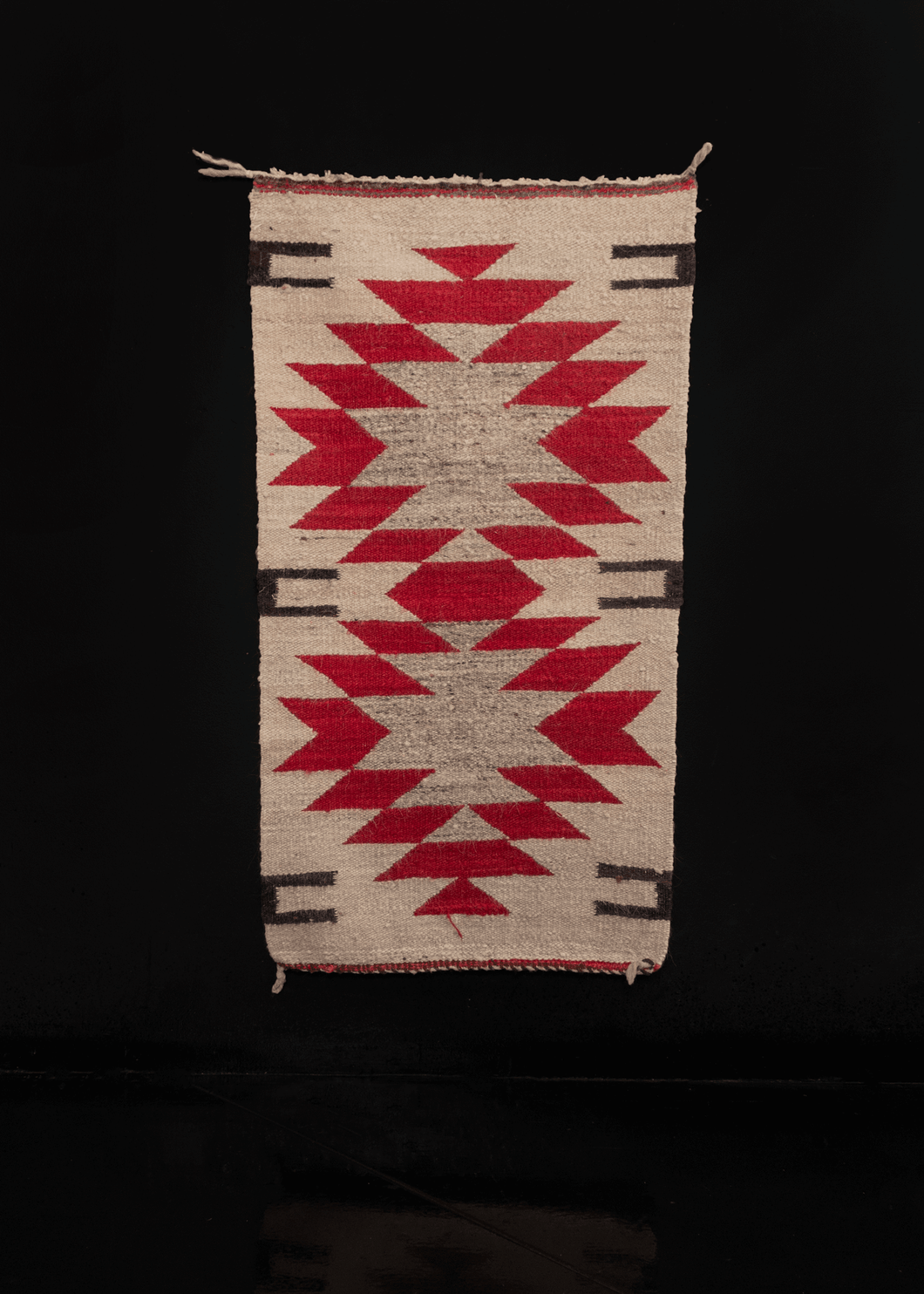 small Navajo rug with geometric design in red and grey on a cream background. 