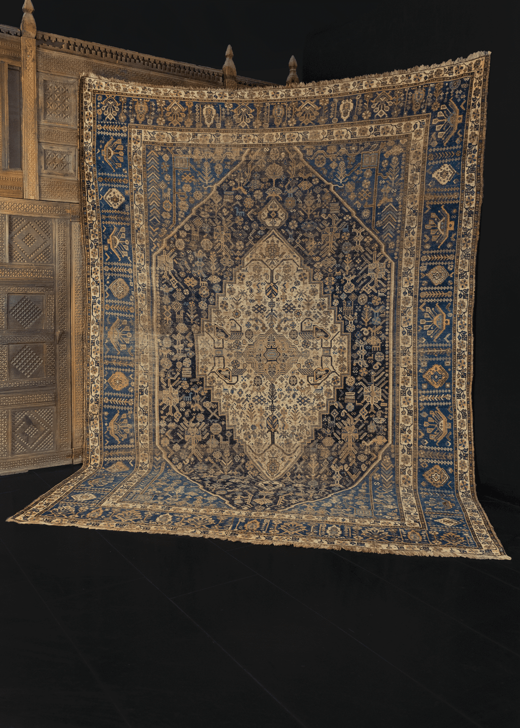 Khamseh rug from S Iran featuring a concentric diamond design with geometric shapes and symbols throughout. The color palette is composed of indigo blues and varying shades of beige. 