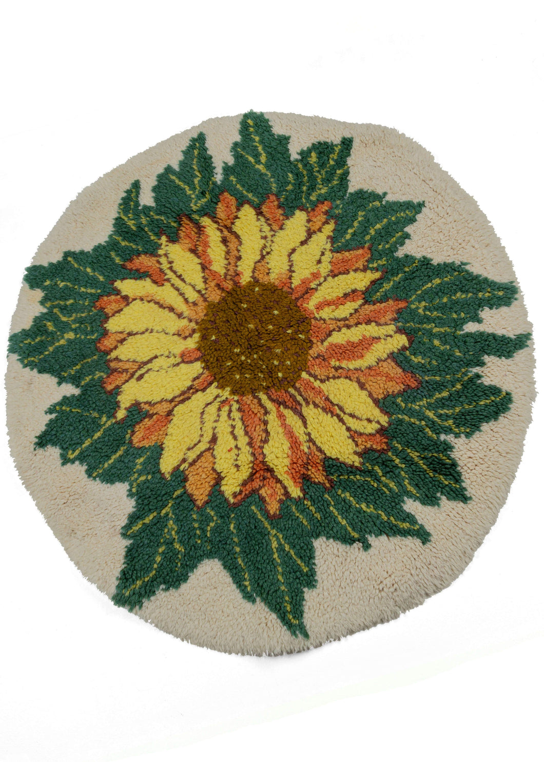 Vintage Latch Hook Sunflower rug that features a top view of a lively sunflower in tones of yellow, oranges and browns atop abundant green leaves and a cream base. The rug is crafted in a hard to find circle which accentuates the roundness of the flower.