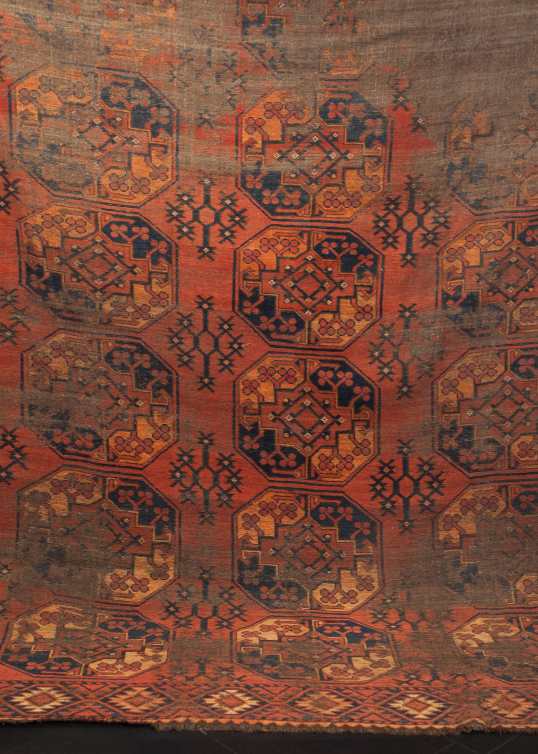 Turkmen rug dating from the 19th century. Earth color palette of brown, red, orange and navy with a repeating gul design. 