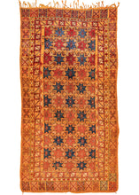 Mid century Moroccan Berber kelleghi shag rug featuring repeating red and blue stars atop a saffron field. It is surrounded by three borders, the most prominent being the large outer border of alternating Xs with ornate C scroll interiors.