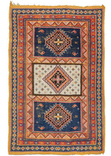 Mid century Moroccan Taznakht area rug featuring a field of three compartments each with a central latch-hooked diamond motif. The center compartment is bright ivory and filled with small protection symbols. The top and bottom compartments feature a more sparse design around a stepped diamond on a navy ground. Of note in the top and bottom compartments are the depiction of oil or "genie" lamps. These are representative of enlightenment either spiritually or intellectually. 