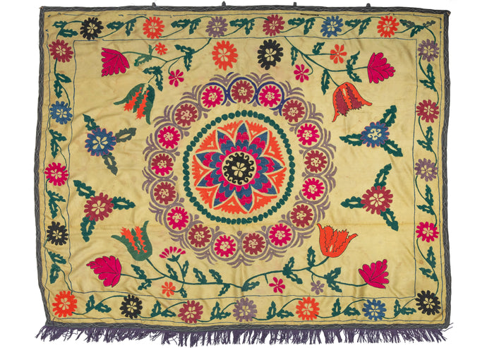 This Vintage Uzbek Suzani features an arrangement of large flowers in bright pink and orange atop a distinctive pastel yellow ground. There are drawn markings visible where the design was left unfinished in places, highlighting the human hand.