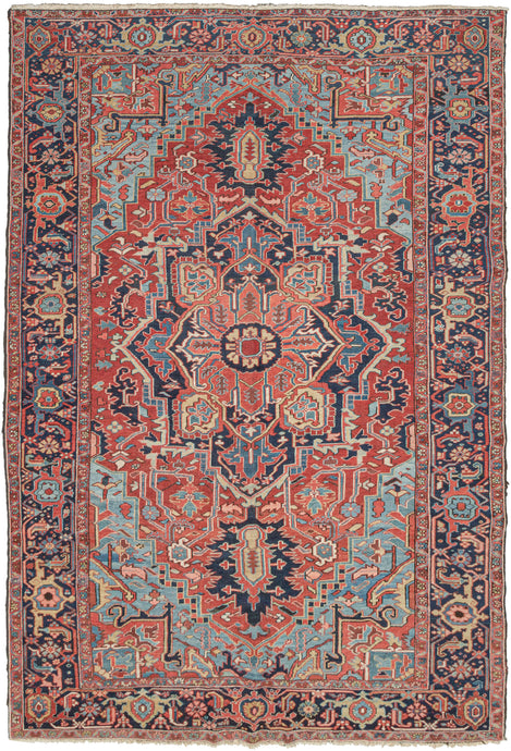 NW Persian Heriz rug featuring a geometric central medallion on rich saturated tones and meaty wool. A brick-red field is complemented by the deep navy, powder blue, yellow, and coral tones with brown and ivory accents. The four powder cornices invigorate the rug and a wonderful undulating abrash adds layers to the composition. It is framed by a main border of alternating palmettes. In a difficult-to-find combo of 7.5' width to 11.5' length.