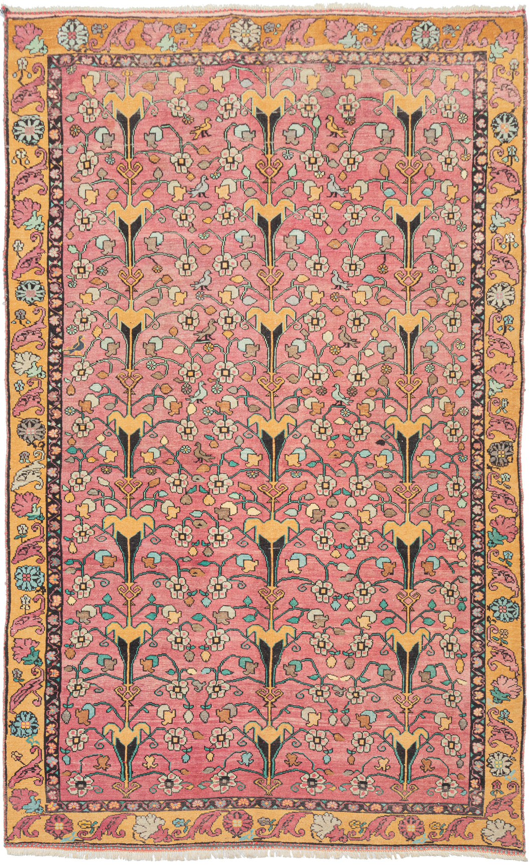 Floral vintage Anatolian Turkish pink & yellow rug featuring an all-over design of stylized vases surrounded by blossoming flowers and small birds in vibrant blues, greens ivory, and gold on a flamingo ground. Surrounded by a main border of rosettes and scrolling leaves on a golden yellow ground.