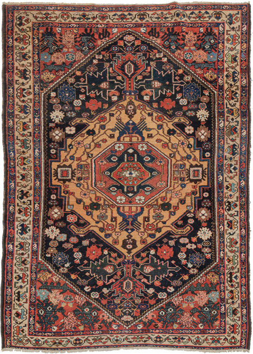 S Persian Bakhtiari rug featuring a concentric central medallion with fields chock full of various rosettes, leaves, and other abstracted forms in tones, red, pink, blue, green, ivory, and a spectacular amber yellow that completely steals the show. The cornices feature interesting speckled forms that are likely stylized vegetal forms but almost feel like mythological beasts. Framed by the main border of meandering palmettes on a camel ground and two minor borders of polychrome elongated PAC-man botehs. 