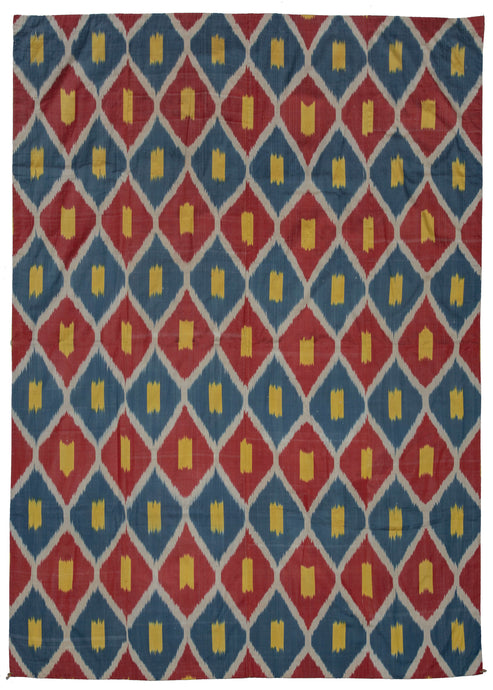 Silk Uzbek handwoven ikat textile featuring a repeating interlocking diamond motif in blue, red, and yellow with a white outline. The back is a brightly colored paisley print on synthetic fabric. 