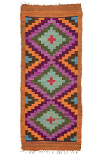 This Vintage Peruvian Kilim features three concentric diamonds with a "+" center and is framed by a plain burnt orange border. The tones are an unexpected combination of various purples and greens with red, orange, and turquoise which create a vibrant contrast in a little rug full of personality.  The colors and style suggest it was woven in the Ayacucho region. Very soft and lightweight, can double as a multifunctional textile or wall tapestry.