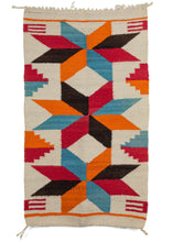 Small Navajo weaving featuring a repeating sunburst pattern in browns, reds, and ivory. A simple brown border frames the simple and elegant jagged diamond motif.