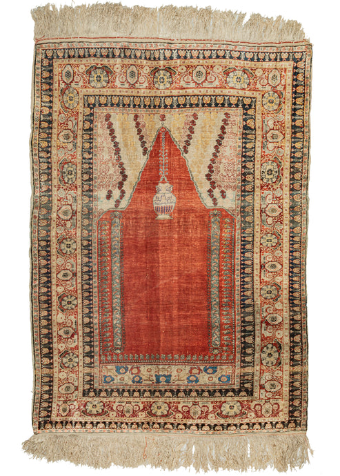 This Antique Silk Turkish Hereke features two columns and a hanging lantern. The mihrab is mostly open with a rich orange tone made more sumptuous when rendered in silk.  The top has two strips with pale yellow patterning that add dynamism and the feel of illumination. Nicely framed by an ornate major and minor border which adds gravitas to the composition. The very precise and dense weave makes this rug exceptionally fine.