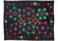 This Vintage Uzbek Suzani features six floral medallions in green, red, yellow, and blue atop a faded black ground. There are drawn markings visible where the design was left unfinished in places, highlighting the human hand.