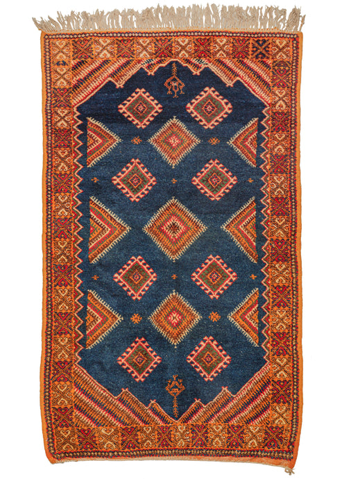 This Vintage Moroccan Rug features a variety of larger concentric and smaller latch hooked diamonds on a midnight blue ground. Diagonally striped cornices add movement and power to an otherwise classic composition. Framed by a nicely contrasting saffron border with accents of red, brown, ivory, blue, and green. 