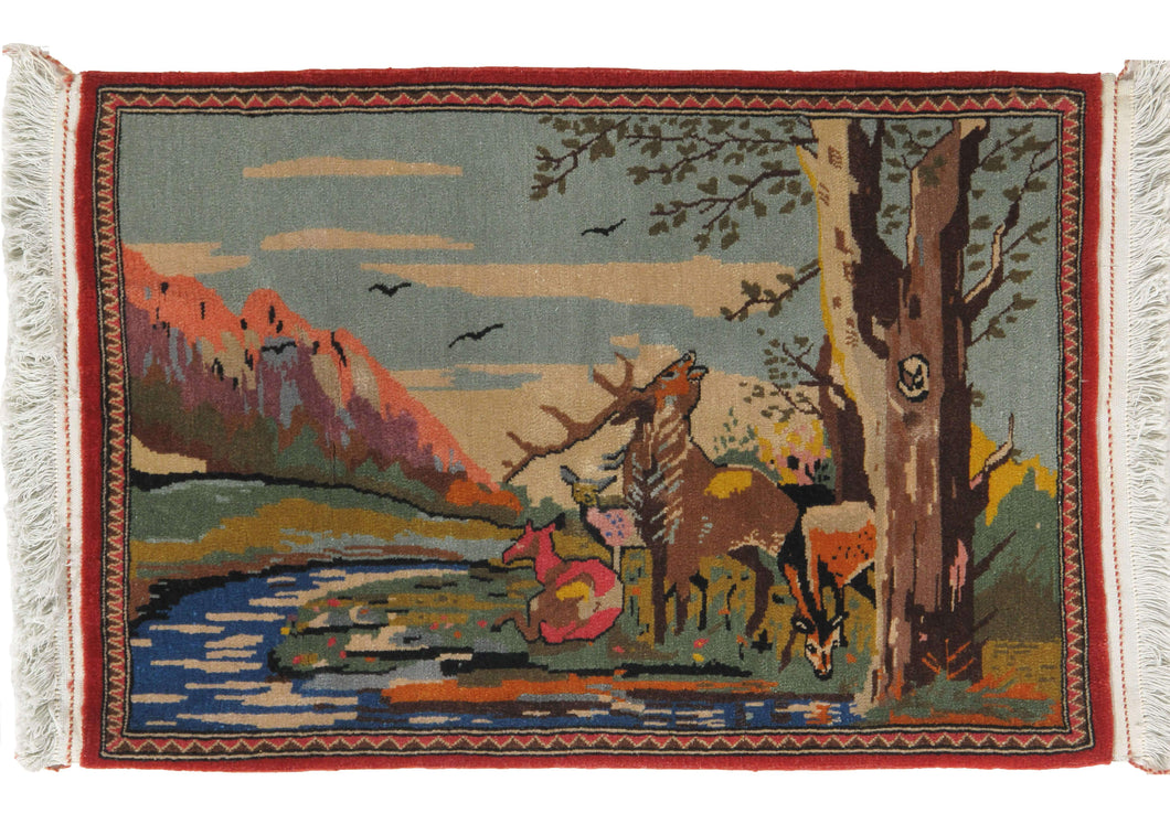 vintage Kashan pictorial rug featuring a sweet and bucolic scene depicting a family of deer by a river underneath a tree. In the distance are mountains and blue skies. Vibrant pinks, blues, and greens bring this wonderful scene to life, and the dainty pink border frames the image.