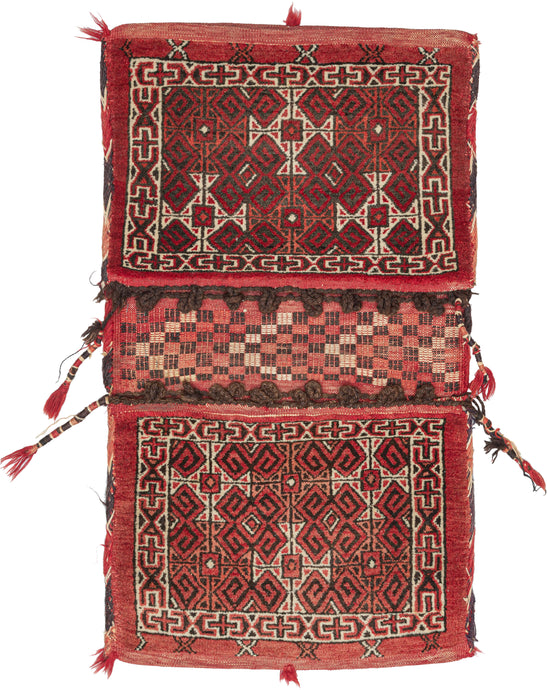 Turkmen Khorjin saddlebag featuring pile front & flatwoven back. Small braided loops at the tops of both bag-faces act as closures. The design of the bag faces is made up of a repeating geometric motif, with a large border, and the kilim between the faces is of squares in alternating colors. The color palette is limited to reds, whites, and browns. 